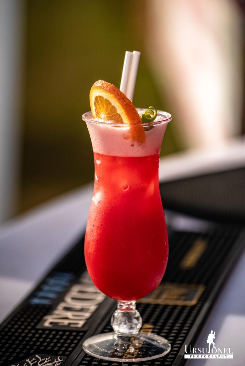 A ruby red ALL 4 BAR cocktail with an orange slice on the bar